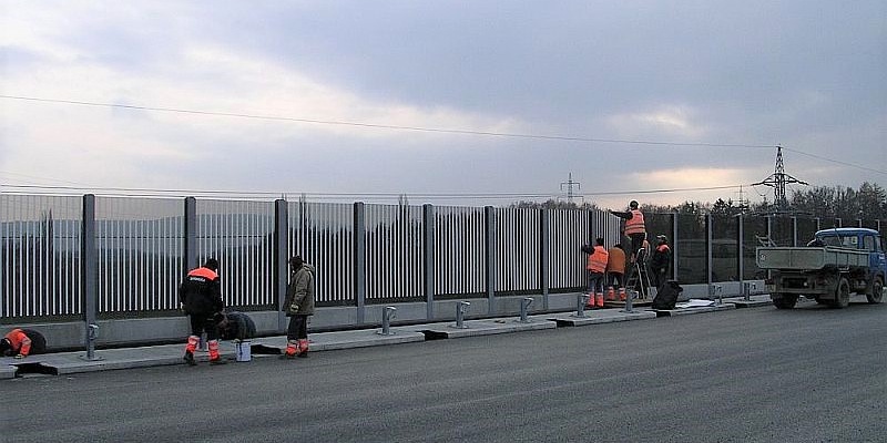 Dělníci, kteří aplikují polepy na protihlukové sklněné stěně na dálnici