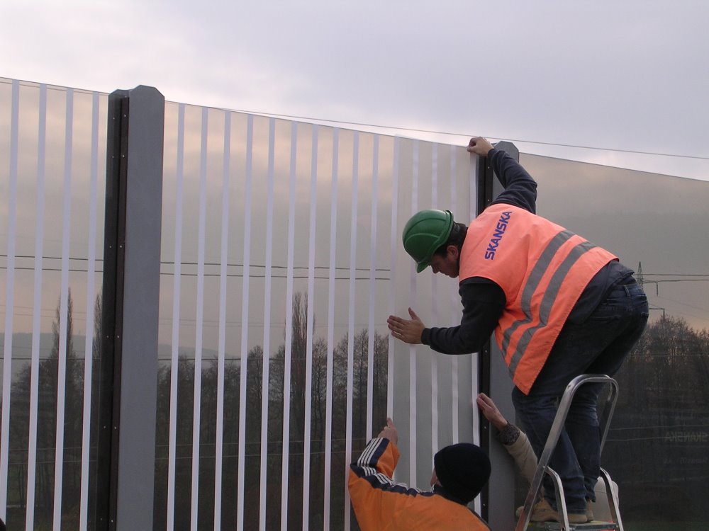 Dělník, který aplikuje polepy na protihlukovou skleněnou stěnu na dálnici.